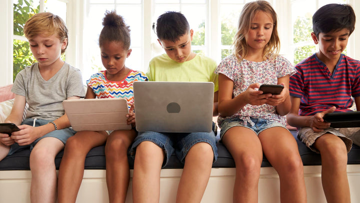 5 children sitting in a window sill all on tech devices. 