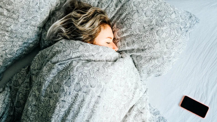 woman sleeping in her bed with cell phone on her bed next to her