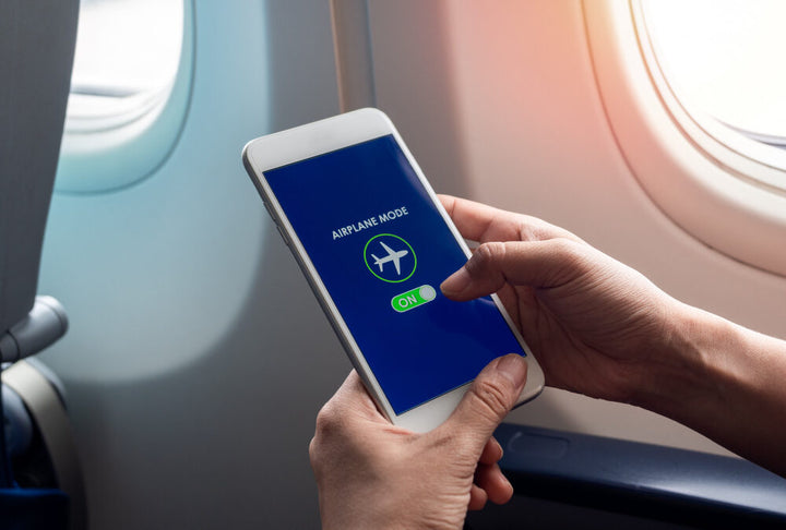 person sitting on an airplane holding cell phone with two hands, showing airplane mode activated